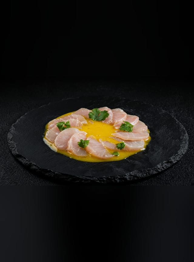 Slices of raw sea bass fanned in a circle over a pool of yellow ají amarillo sauce, scattered with coriander.
